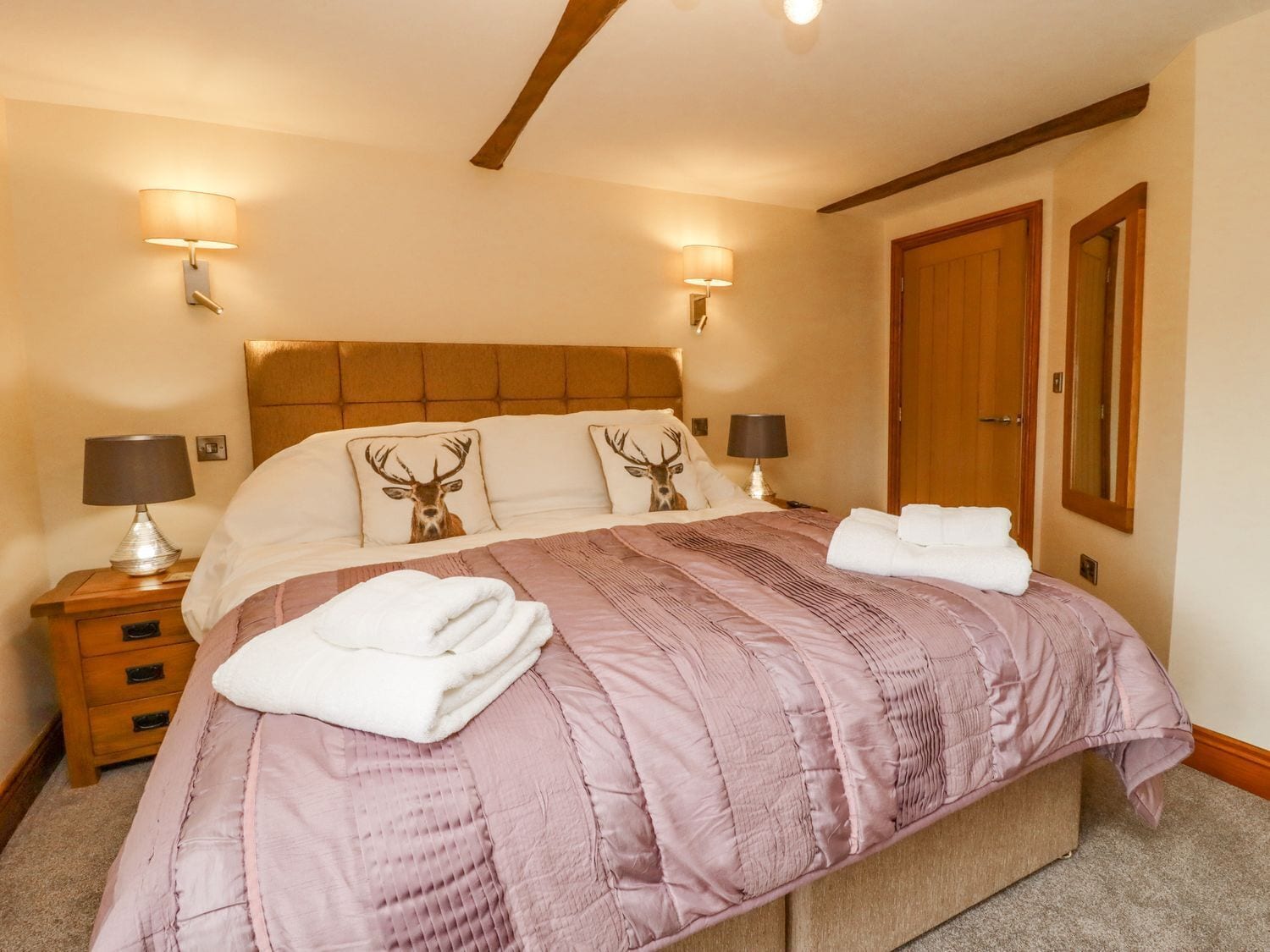 A neatly made bed with a headboard, two bedside lamps, a wooden nightstand, and a wooden door.