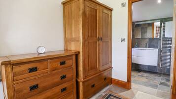 A wooden wardrobe with multiple drawers and a clock on top, a bathroom with a sink and towel rack, and a patterned rug on the floor.