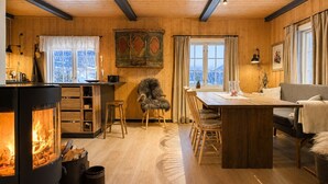 A cozy cabin interior with a central fireplace, wooden walls, a dining area, and a sofa. - Charming mountain retreat in Sudndalen (Hol)