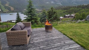 A wooden deck with a wicker sofa and a wood-burning stove, overlooking a lake and mountains. - Charming mountain retreat in Sudndalen (Hol)
