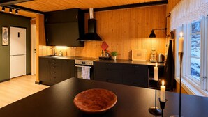 A modern kitchen with wooden walls, a central island, and a view of a snowy landscape. - Charming mountain retreat in Sudndalen (Hol)