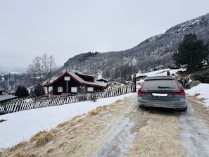 Una strada di campagna con un'auto parcheggiata a lato, una recinzione in legno e una casa con il tetto rosso.