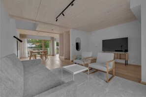 A modern living room with a sofa, chairs, a coffee table, a TV, and a dining area with a table and chairs.