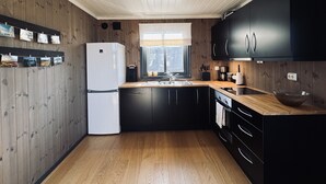 A modern kitchen with wooden walls, a white refrigerator, black cabinets, a wooden countertop, and a window with a view.