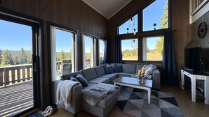 A modern living room with a sectional sofa, a coffee table, and large windows offering a view of a deck and forest.