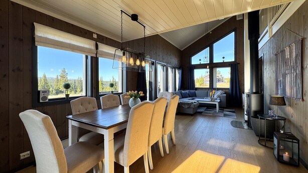 A modern interior with a dining area, sofa, and large windows offering views of the outdoors.