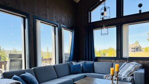 A modern living room with a sectional sofa, a coffee table, and large windows offering a view of the outdoors.