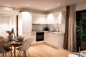 Une cuisine moderne avec des armoires blanches, un four encastré et un coin repas comprenant une table et des chaises blanches.