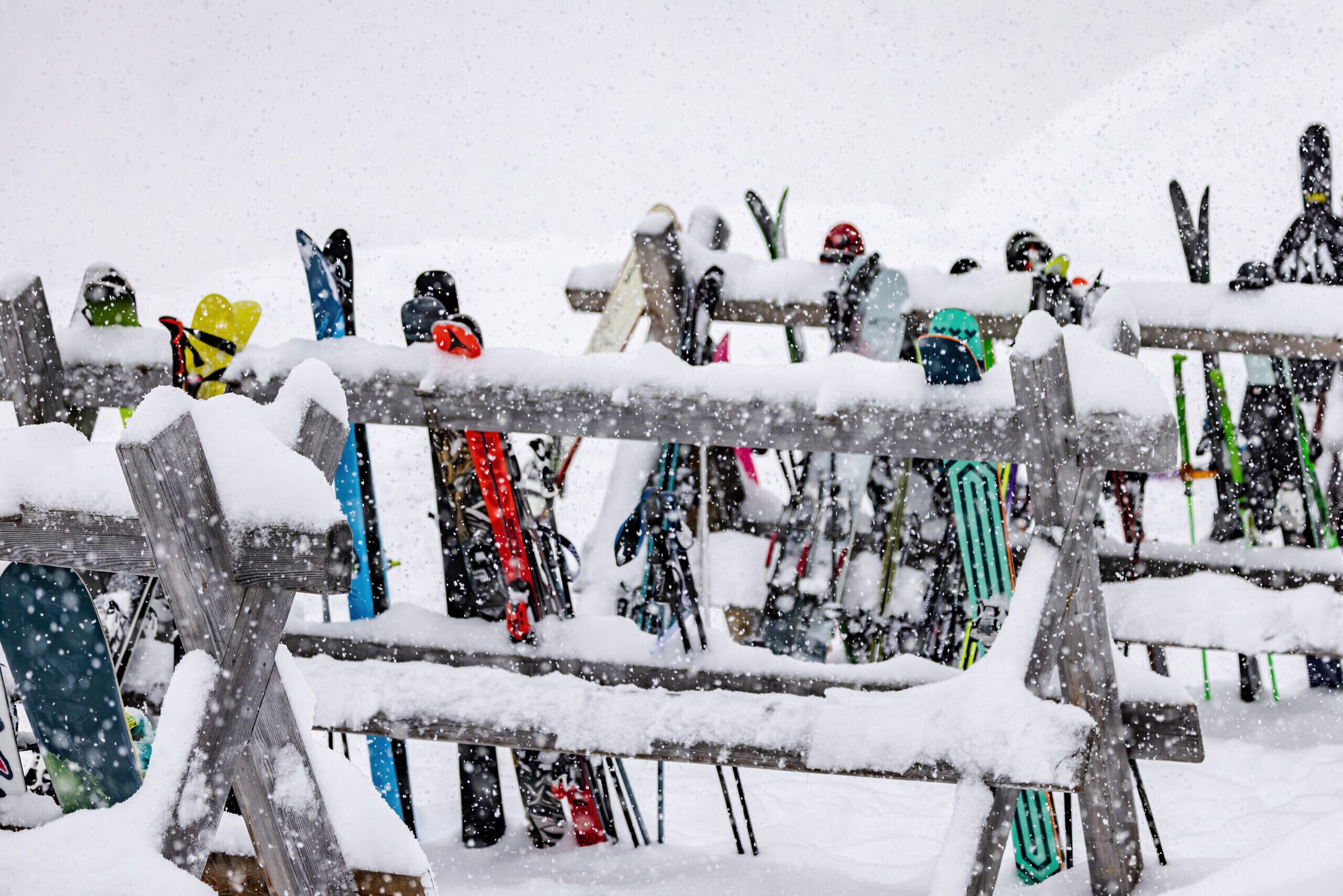 Une clôture en bois, avec des paires de skis et des snowboards recouverts de neige appuyés contre.