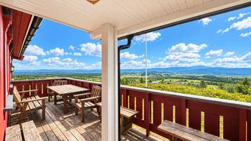 A wooden deck with a table and benches, overlooking a scenic landscape with mountains and fields.