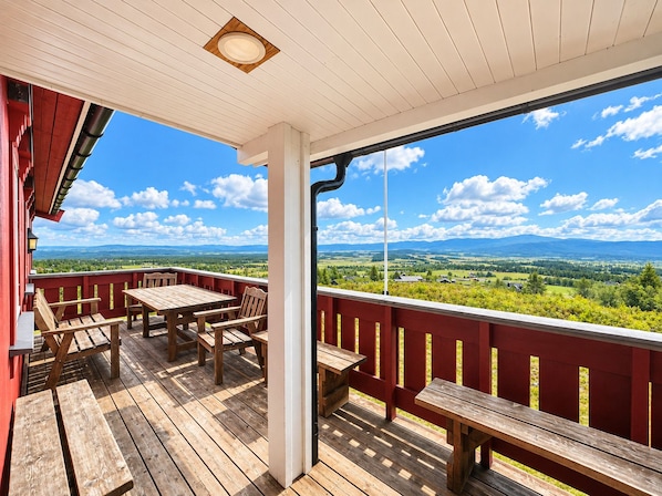 A wooden deck with a table and benches, overlooking a scenic landscape with mountains and fields.