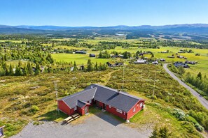 A red building with a gravel driveway and a picnic table in a rural setting with green fields and scattered houses.