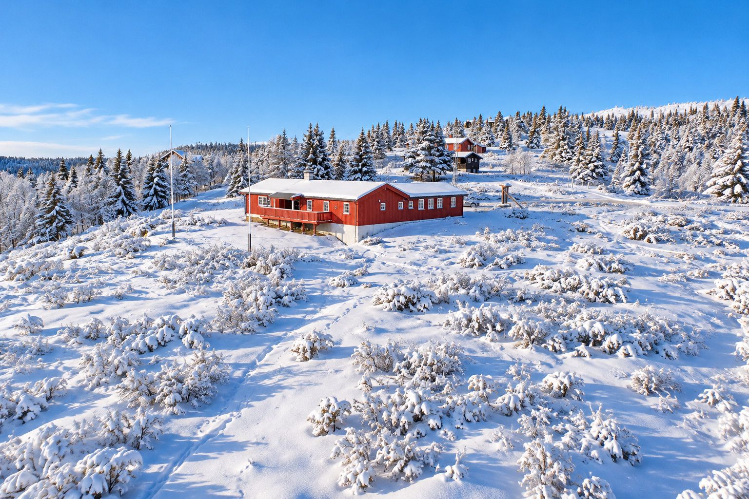 Une cabane rouge, entourée d’arbres couverts de neige, sous un ciel bleu dégagé.