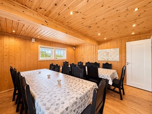 A room with wooden walls and ceiling, a large table with chairs, two windows with a view, and a map on the wall.