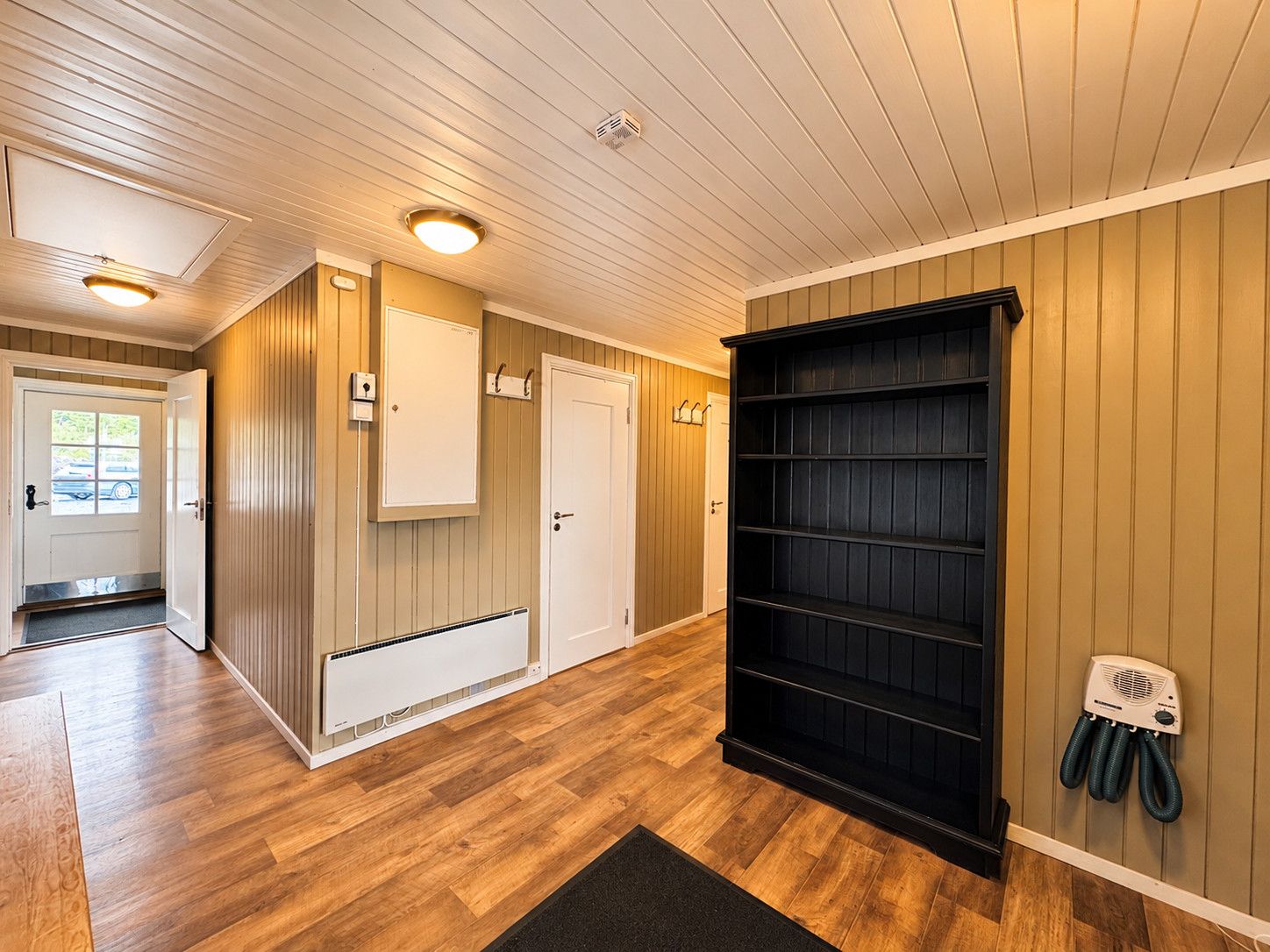 A hallway with wooden floors, a radiator, a black shelving unit, and a door with a window.