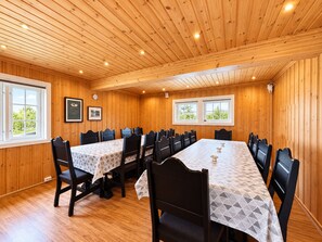 A wooden-paneled room with a long table and chairs, two windows, and framed pictures on the walls.
