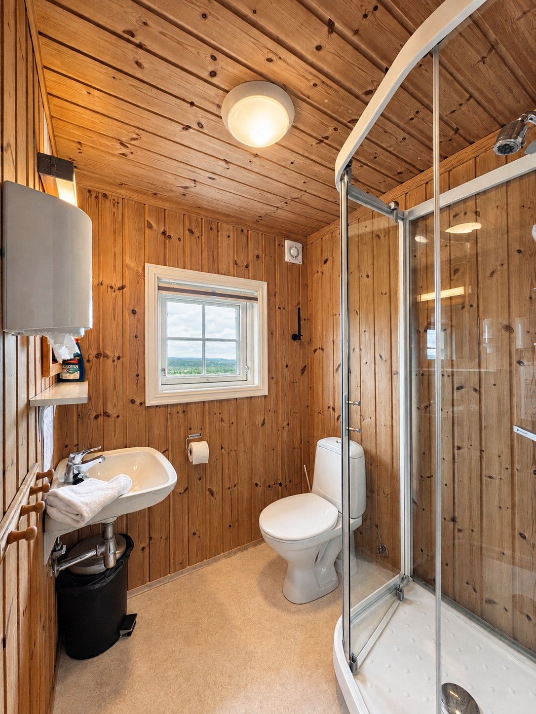 Ein Badezimmer mit Holzwandverkleidung, einem Waschbecken, einer Toilette und einer Duschkabine aus Glas.