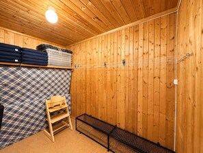 A room with wooden walls, a ceiling light, a bed with a plaid cover, a wooden chair, and a metal rack.