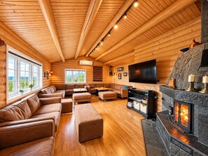 A log cabin interior with a fireplace, seating area, and a large window offering a view.