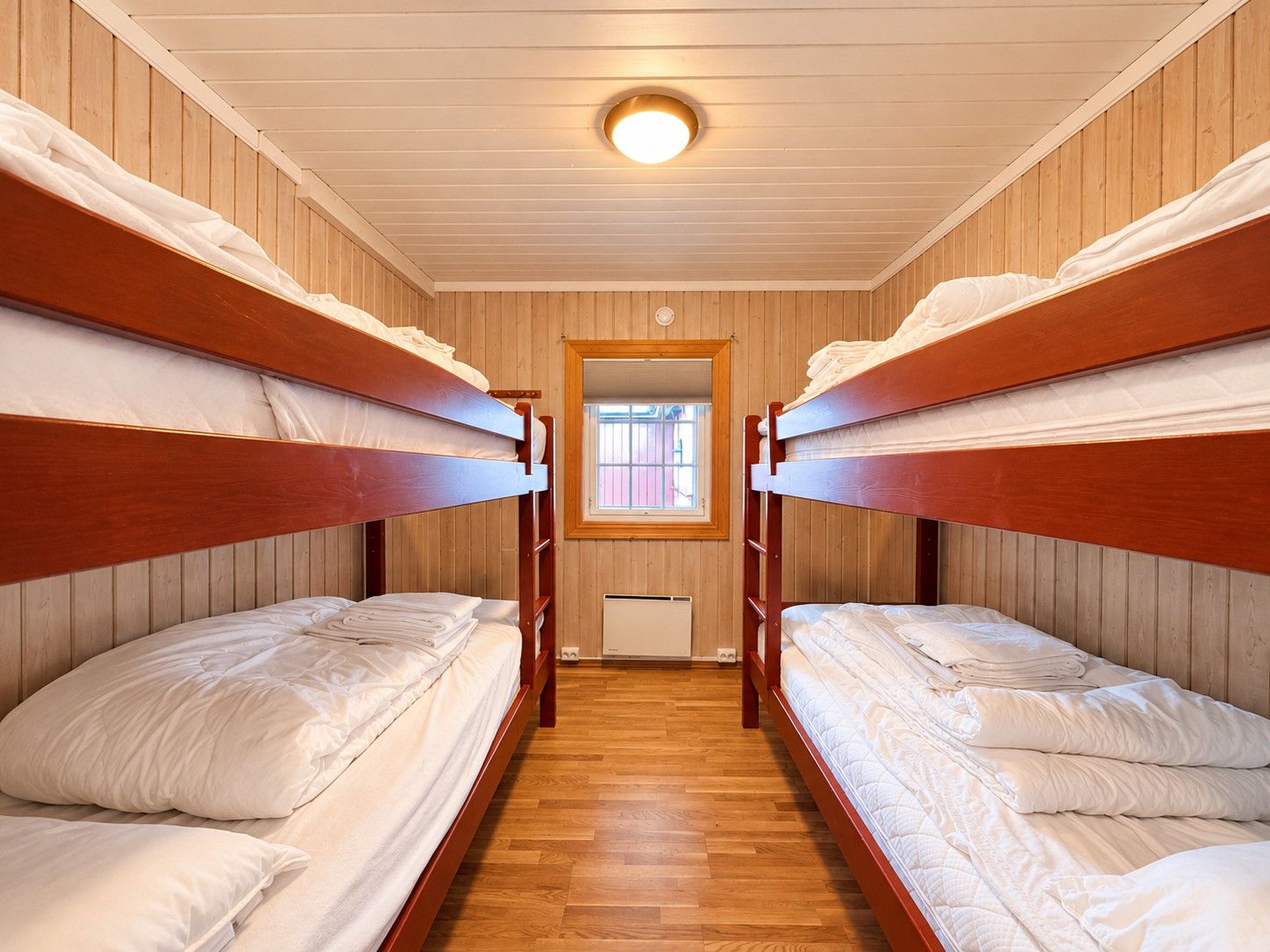 A room with bunk beds, wooden walls, a window, and a ceiling light.