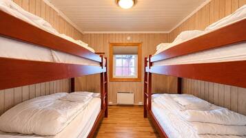 A room with bunk beds, wooden walls, a window, and a ceiling light.