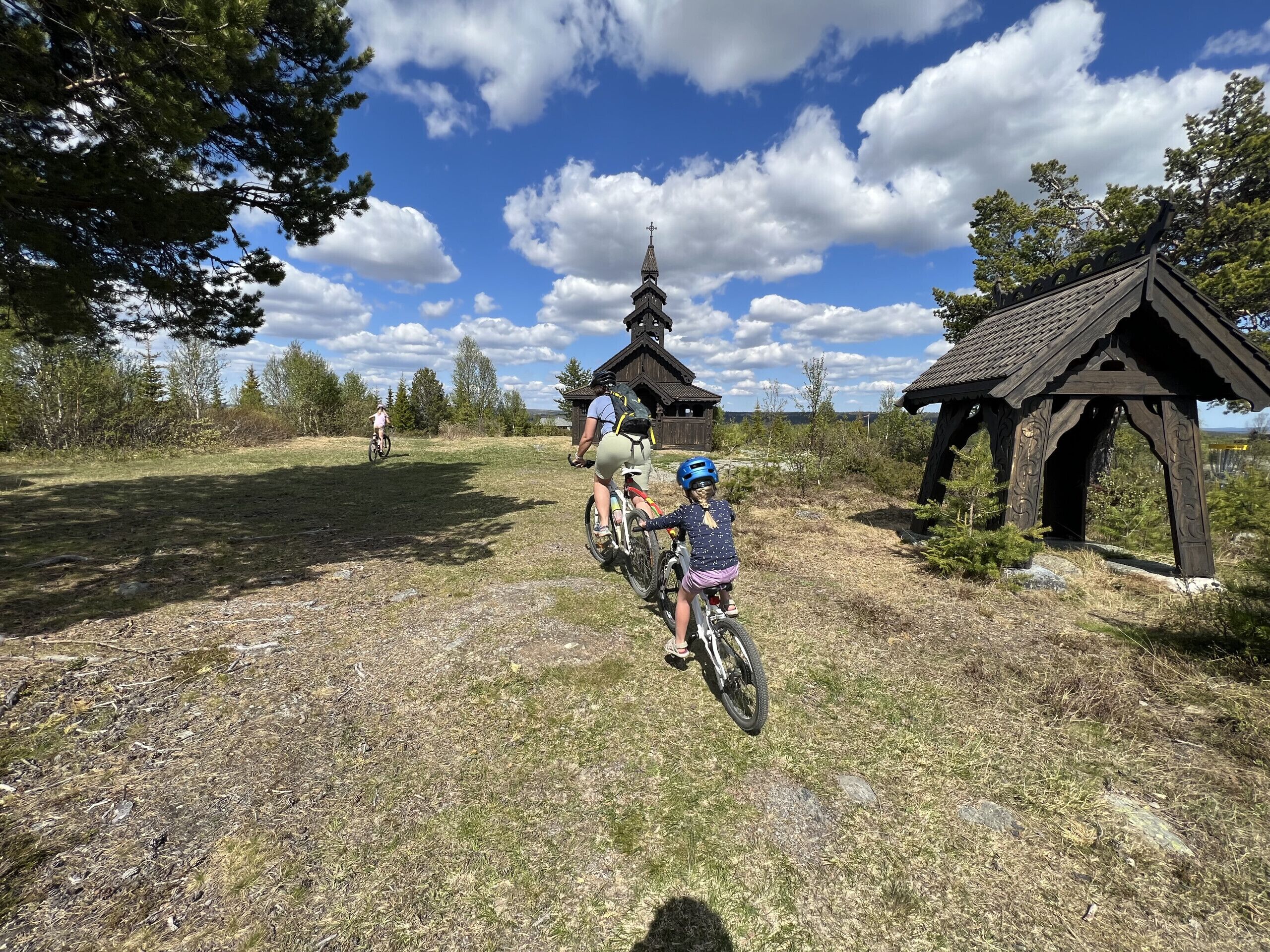 A rural setting with a wooden structure, a small building with a pointed roof, and a clear sky.