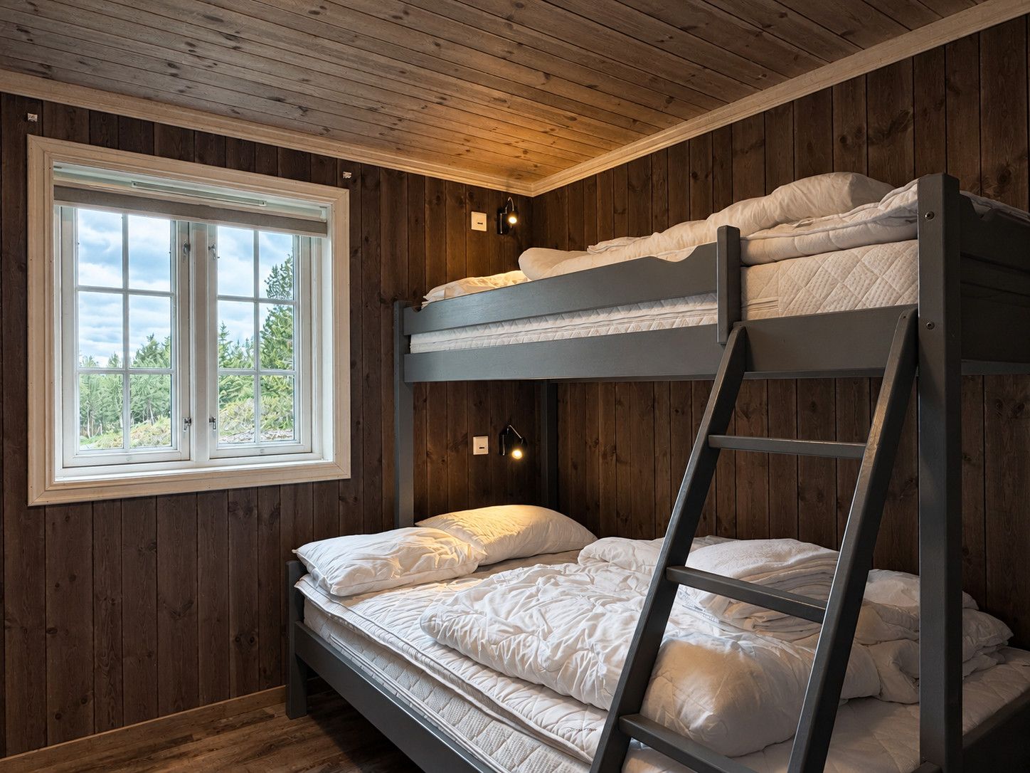 Ein Schlafraum mit Etagenbett, Fenster, Holzwänden und einer Leiter.