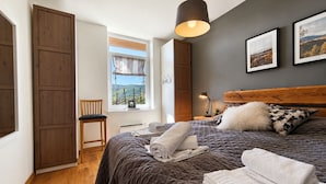 Ein Schlafzimmer mit einem Bett, einem Sessel, einem Fenster mit Aussicht, einem Nachttisch mit Lampe und einer Kopfteil.