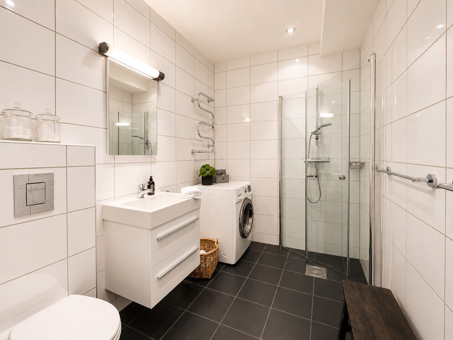 A modern bathroom with a white vanity, a glass shower enclosure, and a washing machine.