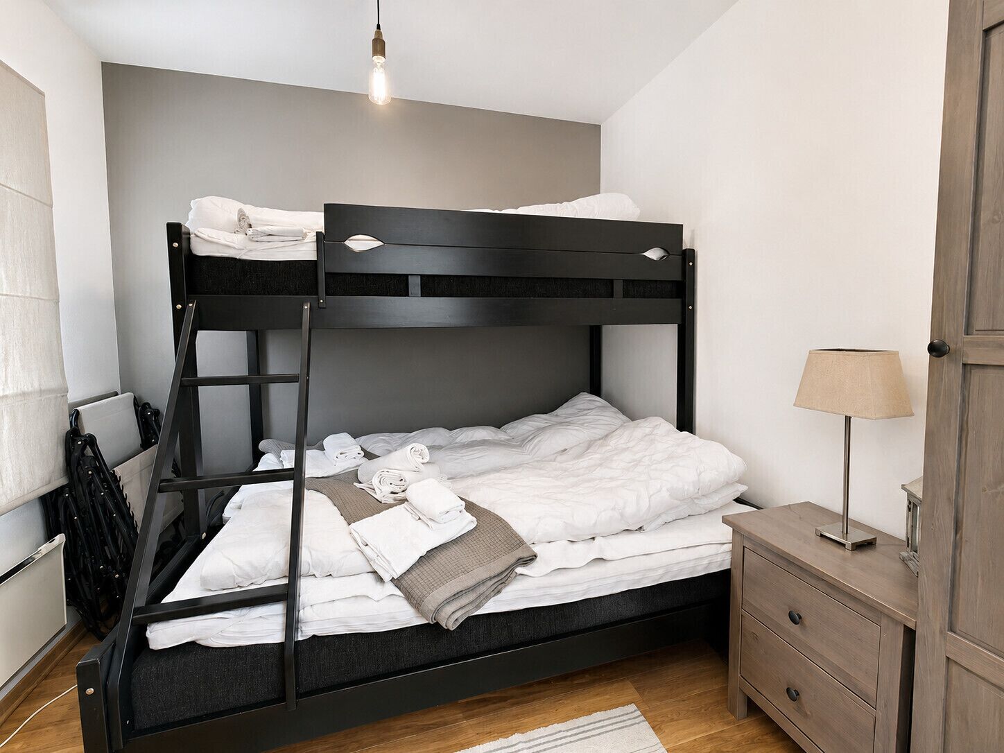 Un letto a castello con una scala, un comodino, una lampada e un pavimento in legno.