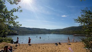 Ein See mit Schwimmern und Spaziergängern am Ufer, umgeben von Hügeln.