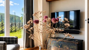 Ein Wohnzimmer mit Fernseher, Blumen in einer Vase, einem karierten Sofa und einem Holztisch.