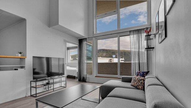 A modern living room with a sofa, coffee table, TV, and large windows offering a view of the outdoors. - Central apartment with seaview, Tromsø (Tromsø)