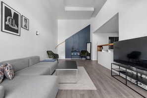 Ett modernt vardagsrum med en grå soffa, ett svart soffbord, en tv på ett svart tv-bord och en trappa som leder till ett annat våningsplan.