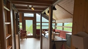 A wooden cabin interior with a dining area, wooden shelves, and a view of the outdoors.