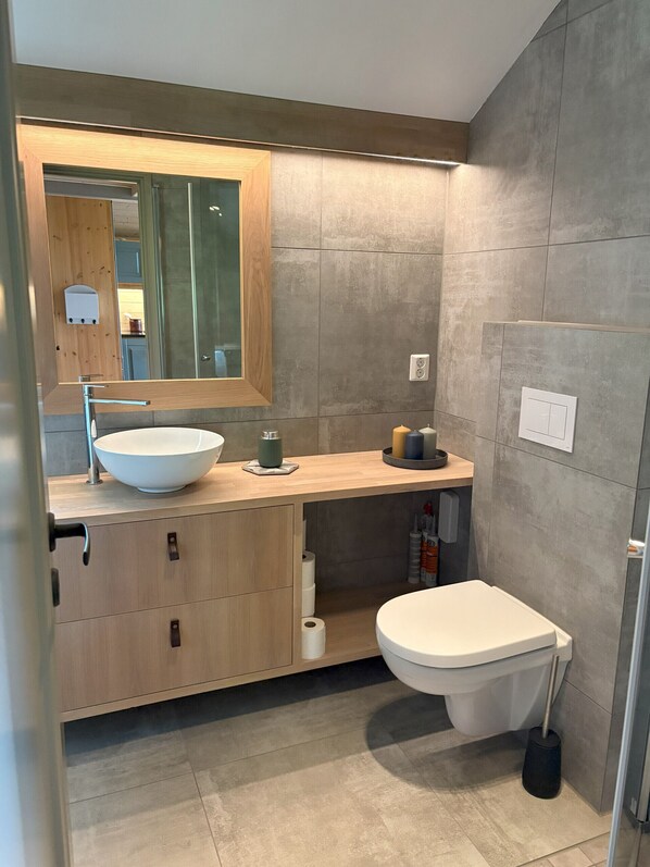 A modern bathroom with a wooden vanity, a large mirror, a white sink, and a toilet.