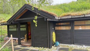 A black wooden cabin with a sloped roof, a covered porch, and a stone pathway leading to the entrance.