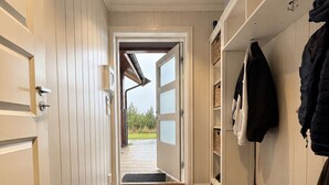 A hallway with a door leading outside, a mat at the entrance, and a coat rack with jackets.
