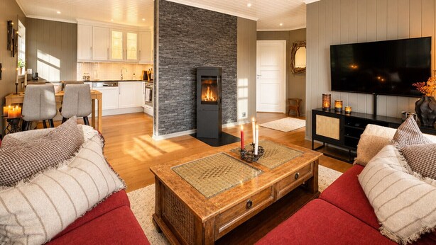 A modern living room with a fireplace, a television, and a kitchen in the background.