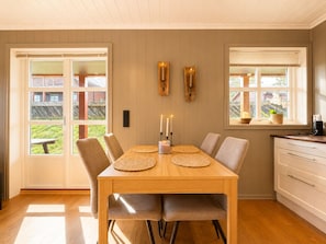 A dining area with a wooden table, six chairs, two wall-mounted lights, and a view through a glass door to the outside.