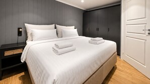 A modern bedroom with a large bed, dark wooden wardrobe, and a white door.