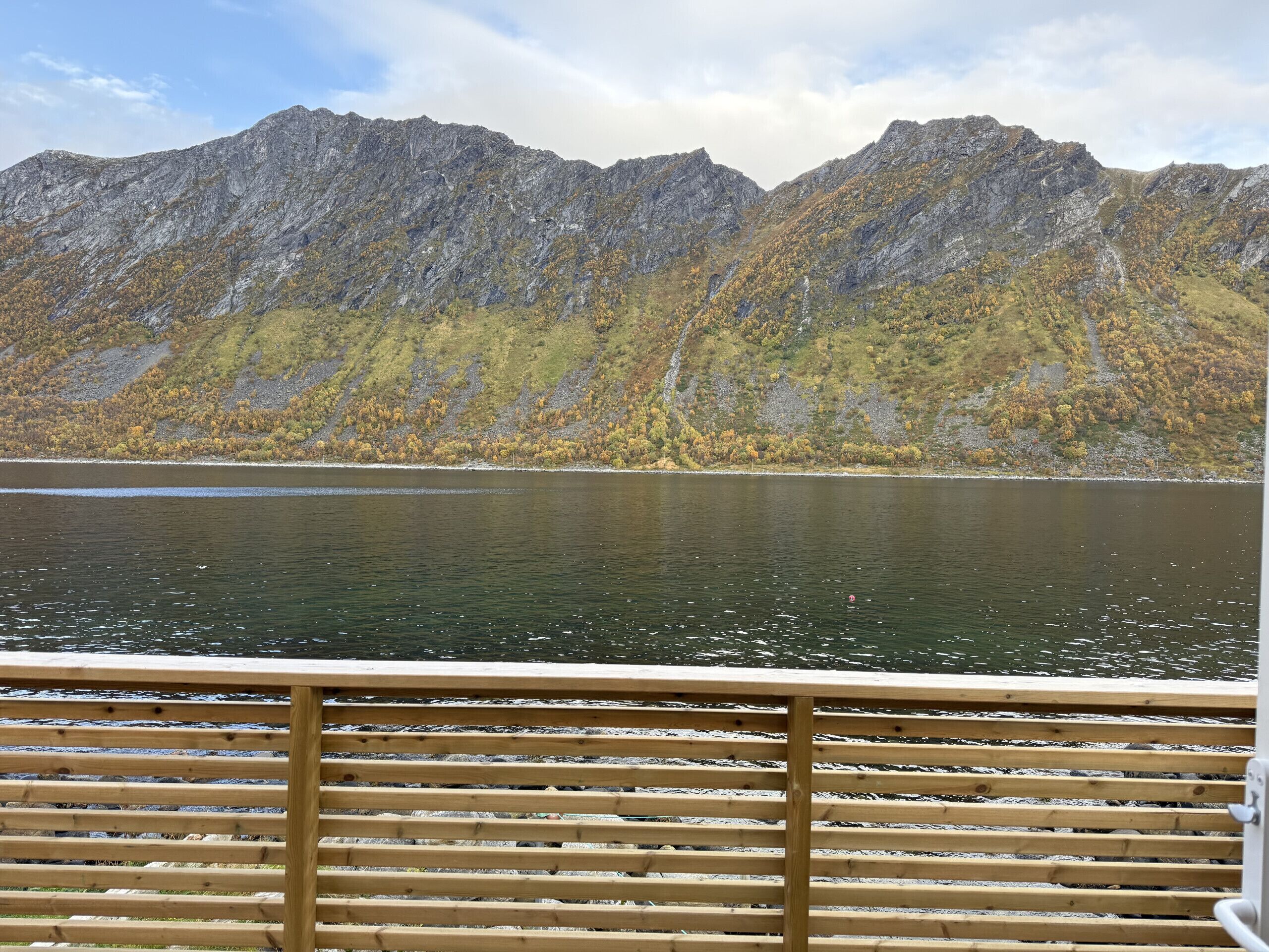 Ein See mit Bergen im Hintergrund und einer Holzterrasse im Vordergrund.