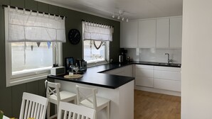 Una cocina moderna con armarios blancos, una isla central y un comedor con sillas blancas.