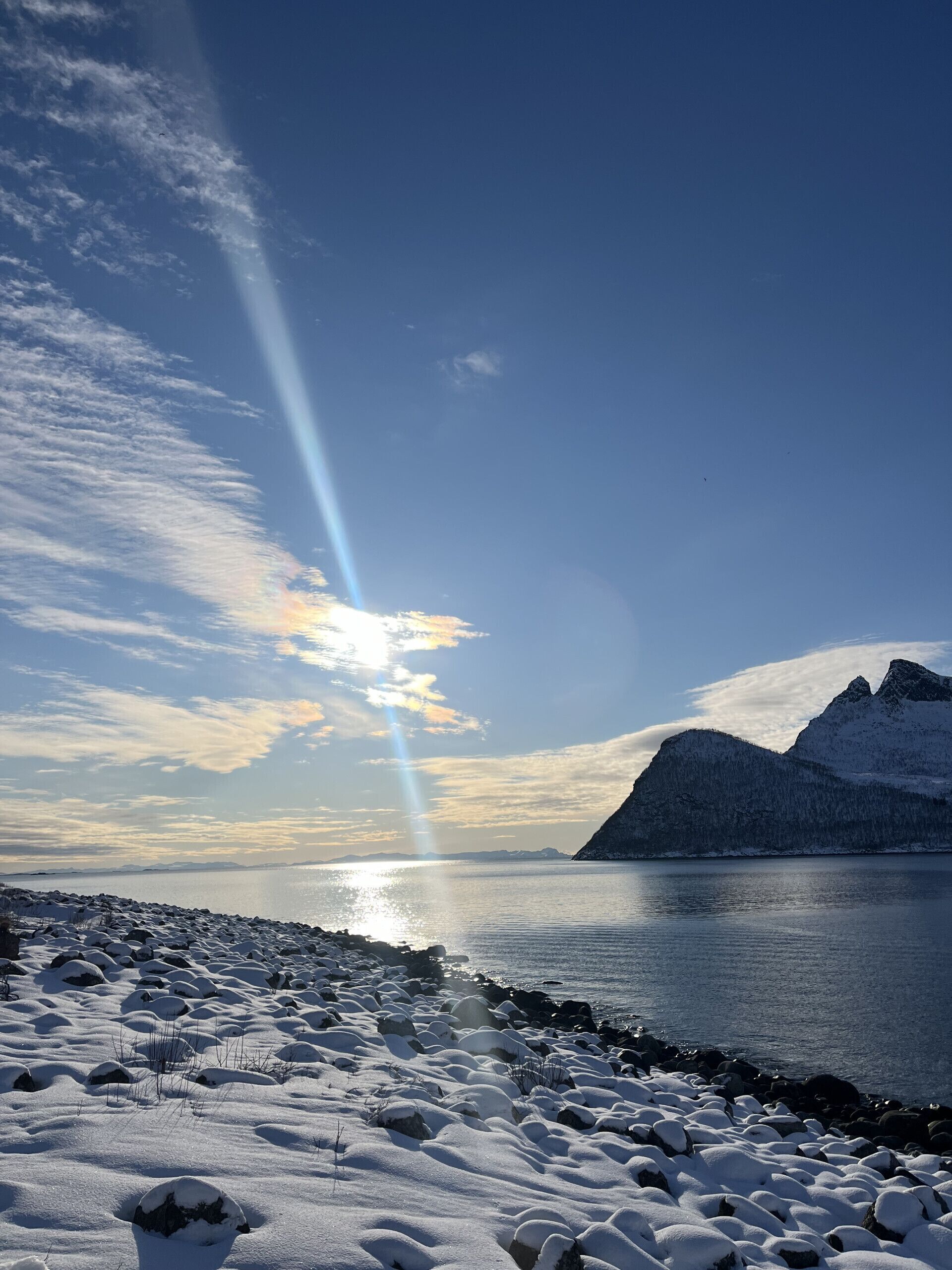 Schneebedeckte Landschaft mit einem stillen See, fernen Bergen und blauem Himmel.