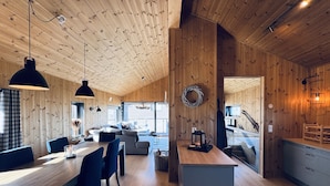 A modern interior with wooden walls, a dining area with a table and chairs, a sofa, and a kitchen area with a counter and appliances. - Moderne leilighet i Vestlia . Ski in ski out (Hol)