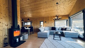 A cozy cabin interior with a fireplace, a dining area, a living room with a sofa, and large windows. - Moderne leilighet i Vestlia . Ski in ski out (Hol)