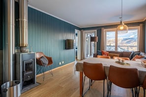 A modern interior with a wood-burning stove, a dining area with a table and chairs, a sofa, and a large window with a view.