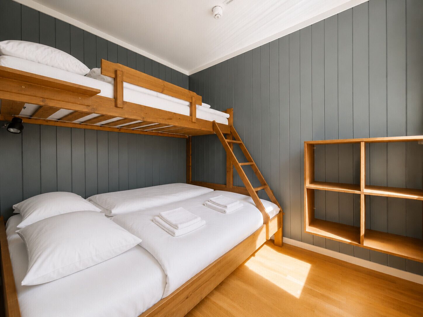 A bunk bed with a wooden ladder, a shelf unit, and a ceiling light fixture.