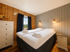 Une chambre avec deux lits, une commode, une table de chevet et une fenêtre avec des rideaux.