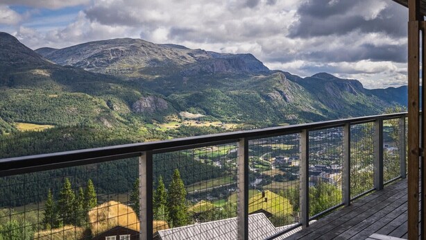 A balcony with a metal railing overlooking a mountainous landscape with a town below.